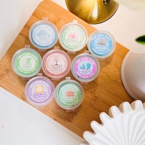 May include: Eight small, round, clear plastic containers with colourful labels from The Glow Barn. Labels feature text including Glass Slipper, Golden Afternoon, Oceania, Pixie Dust, Walt's Office, Under The Sea, Floating Lanterns, and Carl & Ellie's Picnic.