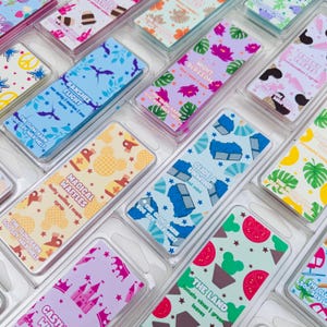 K&ouml;nnte beinhalten: Eine Sammlung rechteckiger Sojawachs-Duftwachsstangen in transparenter Kunststoffverpackung, jede mit einzigartigen farbenfrohen Mustern und Etiketten mit Namen wie Banshee Flight, Night Blossom, Magical Waffles, Glide & Unwind und The Land.