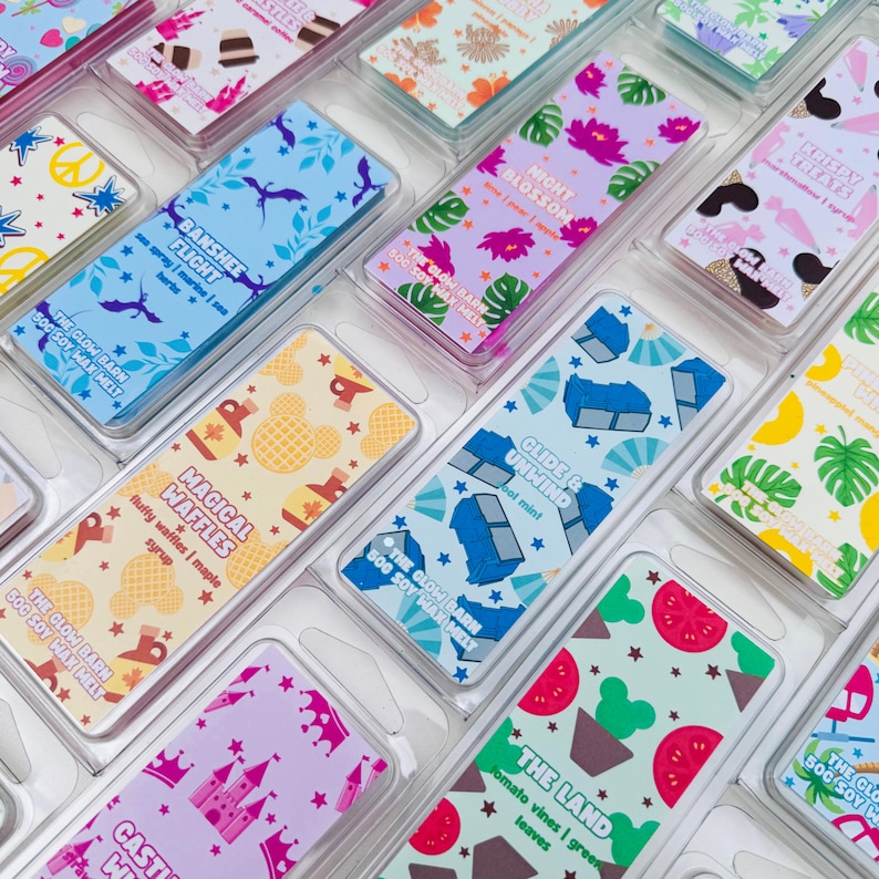 K&ouml;nnte beinhalten: Eine Sammlung rechteckiger Sojawachs-Duftwachsstangen in transparenter Kunststoffverpackung, jede mit einzigartigen farbenfrohen Mustern und Etiketten mit Namen wie Banshee Flight, Night Blossom, Magical Waffles, Glide & Unwind und The Land.