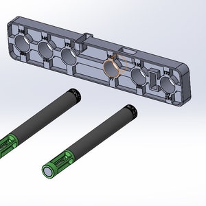 Pode incluir: Um componente de plástico cinza com aberturas circulares e números. Dois objetos cilíndricos pretos e verdes abaixo. Os objetos cilíndricos têm uma pega texturizada. Medidas em milímetros.