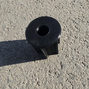 Op de afbeelding: Een zwart kunststof onderdeel met een cirkelvormige bovenkant en een centraal gat. Het onderdeel heeft een cilindrische vorm met een platte basis en maakt waarschijnlijk deel uit van een grotere assemblage.