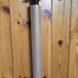 May include: A black plastic wrap dispenser with a textured handle and a circular base. The dispenser holds a roll of clear plastic wrap. The dispenser is against a wooden background.