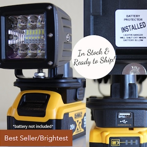 May include: A black LED work light mounted on a yellow and black battery pack. The light has multiple LED bulbs and the text "Best Seller/Brightest". The battery pack has a USB port and the text "DEWALT". A sticker reads "BATTERY PROTECTOR INSTALLED".
