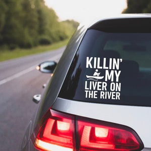 Könnte beinhalten: Ein silbernes Auto mit einem weißen Vinyl-Aufkleber auf der Heckscheibe, auf dem "Killin' My Liver On The River" steht, mit einer kleinen Grafik einer Person in einem Kanu.