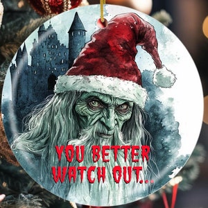 Puede incluir: Un adorno navideño redondo con una ilustración de acuarela de un Papá Noel espeluznante con una larga barba blanca y un gorro rojo. El fondo es un castillo oscuro con un aspecto brumoso y brumoso. El texto "You Better Watch Out..." está escrito en rojo en la parte inferior del adorno.