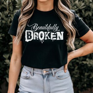 May include: A black t-shirt with white text that reads "Beautifully Broken". The text has a dripping paint effect.