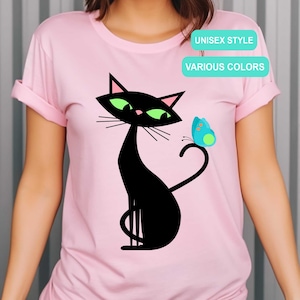 May include: Pink t-shirt featuring a black cat with green eyes and a blue butterfly. The shirt has the text "UNISEX STYLE" and "VARIOUS COLORS".