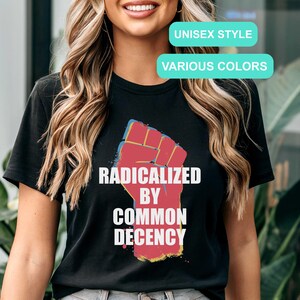 May include: Black t-shirt featuring a red, yellow, and blue fist graphic with the words "RADICALIZED BY COMMON DECENCY" in white. The shirt also has text that says "UNISEX STYLE" and "VARIOUS COLORS".