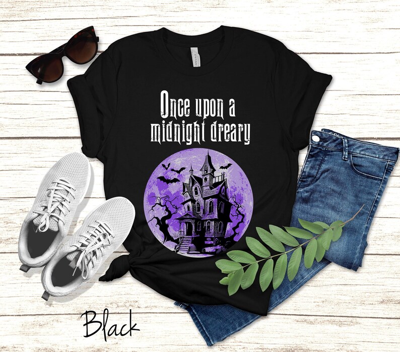 Op de afbeelding: Zwart T-shirt met een paarse maan en een zwart silhouet van een spookhuis. De tekst "Once upon a midnight dreary" staat op het shirt gedrukt.