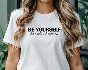 May include: White t-shirt with black text that reads "BE YOURSELF the world will catch up".
