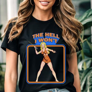 May include: Black t-shirt with a graphic of a woman in a jungle outfit holding a spear. The text "The Hell I Won't" is printed above the graphic.