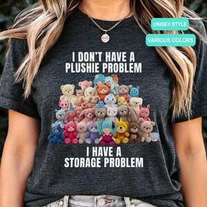 May include: Dark gray unisex t-shirt with the text "I DON'T HAVE A PLUSHIE PROBLEM I HAVE A STORAGE PROBLEM." The shirt features a graphic of various plush toys in different colors. The shirt also has the text "UNISEX STYLE" and "VARIOUS COLORS."