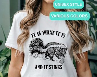 May include: White t-shirt with a black and white illustration of a skunk and the text "It is what it is and it stinks".