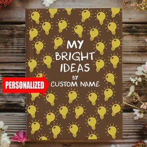 May include: A brown notebook featuring a pattern of yellow light bulbs. The cover displays the text "MY BRIGHT IDEAS" and space for a custom name. A red banner with the word "PERSONALIZED" is on the left.