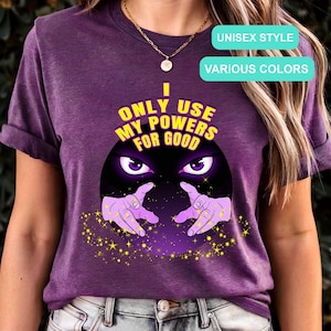 May include: A purple unisex t-shirt with the text "I ONLY USE MY POWERS FOR GOOD" in yellow and black. The graphic features a crystal ball with purple eyes and hands, surrounded by yellow stars. The shirt is available in various colors.