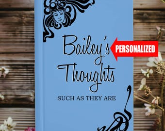 Könnte beinhalten: Ein hellblauer Journal-Umschlag mit einer schwarz-weißen Illustration eines Frauenkopfes und einem floralen Design. Der Text "Bailey's Thoughts SUCH AS THEY ARE" ist auf dem Umschlag gedruckt. Das Wort "PERSONALISIERT" ist in Rot auf einem weißen Pfeil gedruckt.