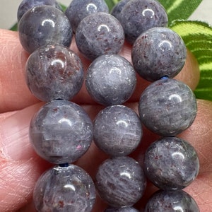 Pode incluir: Um fio de contas redondas de pedra preciosa cinza e branca com um leve brilho iridescente. As contas s&atilde;o enfiadas em um cord&atilde;o azul escuro.