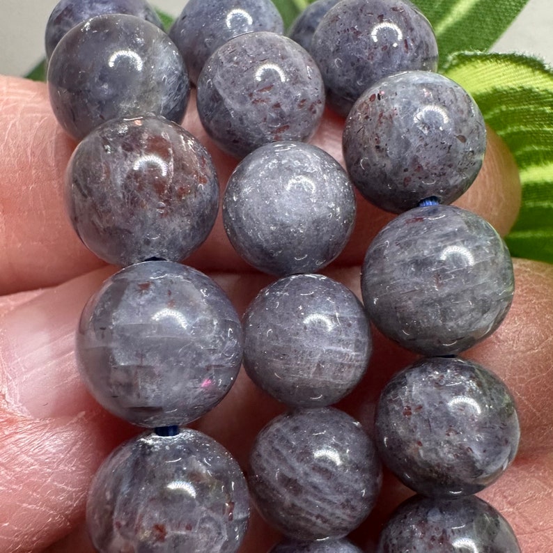 Pode incluir: Um fio de contas redondas de pedra preciosa cinza e branca com um leve brilho iridescente. As contas s&atilde;o enfiadas em um cord&atilde;o azul escuro.