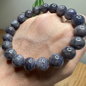 Pode incluir: Um bracelete de pedras preciosas de cor roxo escuro com contas redondas. O bracelete &eacute; feito de pedras naturais e tem um acabamento polido.