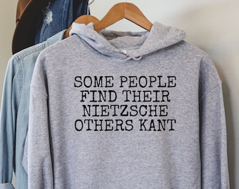 May include: A gray hooded sweatshirt with the text "SOME PEOPLE FIND THEIR NIETZSCHE OTHERS KANT" printed in black.