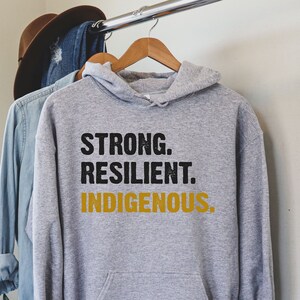 May include: Gray hooded sweatshirt with the text "STRONG. RESILIENT. INDIGENOUS." in black and gold lettering.