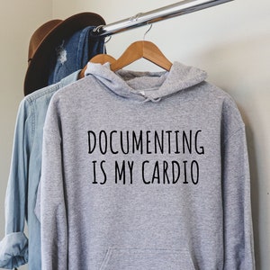 May include: Gray hooded sweatshirt with the text "Documenting is my cardio" printed in black.