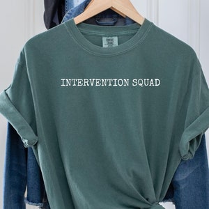 May include: A green t-shirt with the text "Intervention Squad" printed in white on the front.