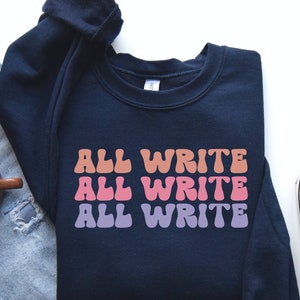 May include: A navy blue sweatshirt with the text "ALL WRITE" repeated three times in a retro font. The text is in shades of pink, orange, and purple.