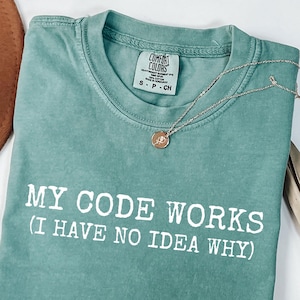 May include: A teal blue t-shirt with the text "MY CODE WORKS (I HAVE NO IDEA WHY)" printed in white.