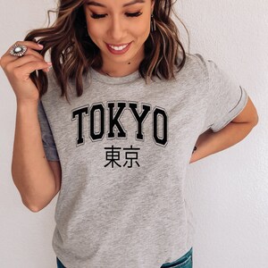 K&ouml;nnte beinhalten: Ein graues T-Shirt mit dem Wort "TOKYO" in schwarzen Blockbuchstaben und den japanischen Schriftzeichen f&uuml;r "Tokyo" darunter.