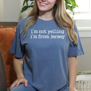 May include: A blue t-shirt with white text that reads "i'm not yelling i'm from jersey".