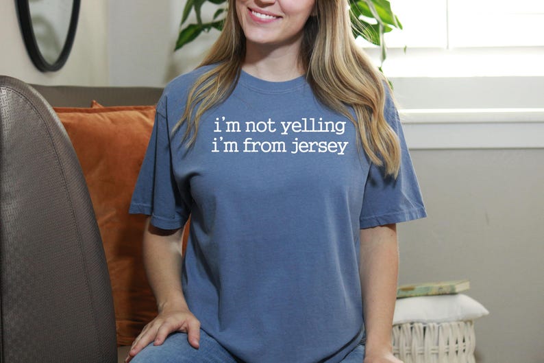 May include: A blue t-shirt with white text that reads "i'm not yelling i'm from jersey".
