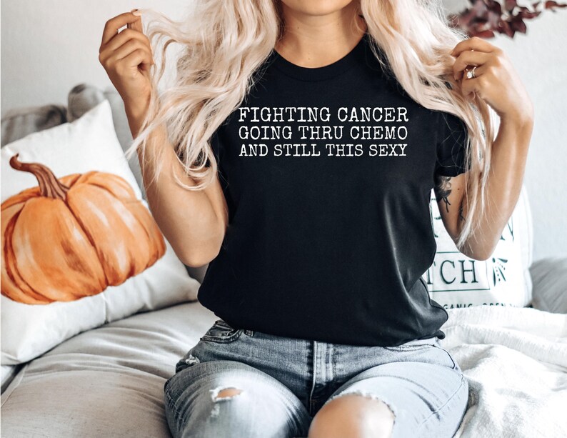 Op de afbeelding: Zwart T-shirt met witte tekst die "Fighting Cancer Going Thru Chemo And Still This Sexy" zegt