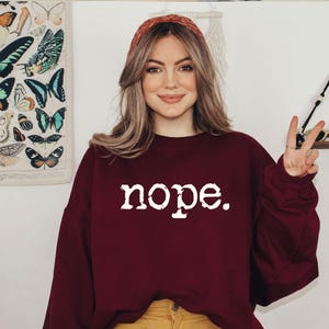 May include: A burgundy sweatshirt with the word "nope" in white lettering. The person is wearing a red headband and yellow pants. A butterfly print is visible in the background.