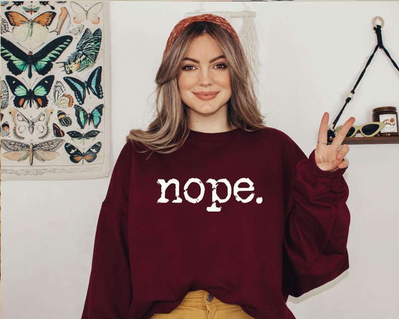 May include: A burgundy sweatshirt with the word "nope" in white lettering. The person is wearing a red headband and yellow pants. A butterfly print is visible in the background.