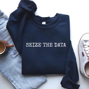 K&ouml;nnte beinhalten: Ein marineblauer Pullover mit dem Text "SEIZE THE DATA" in wei&szlig;en Buchstaben.