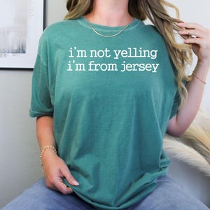 May include: A teal green t-shirt with the text "i'm not yelling i'm from jersey" in white.