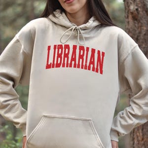 May include: A beige hoodie with a red "LIBRARIAN" graphic printed on the front.