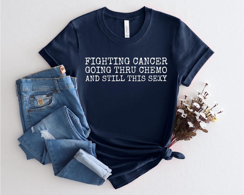 Op de afbeelding: Donkerblauw T-shirt met witte tekst die "Fighting Cancer Going Thru Chemo And Still This Sexy" luidt.