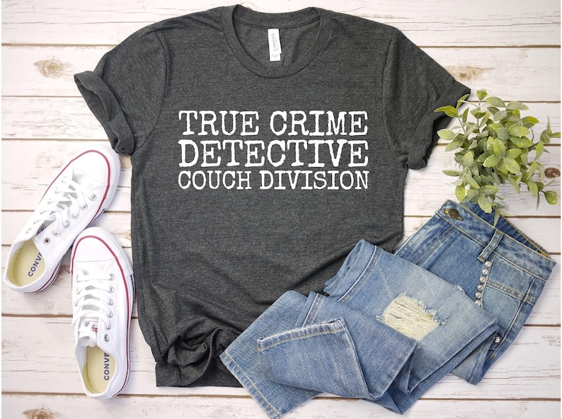 K&ouml;nnte beinhalten: Ein dunkelgraues T-Shirt mit dem Aufdruck "TRUE CRIME DETECTIVE COUCH DIVISION" in wei&szlig;.