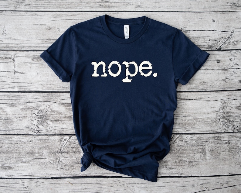 May include: A navy blue t-shirt with the word "nope" printed in white on the front. The word is in a vintage typewriter font.