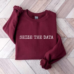 K&ouml;nnte beinhalten: Burgunderfarbener Pullover mit dem Text "SEIZE THE DATA" in wei&szlig;en Buchstaben.