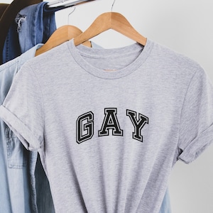 May include: A gray t-shirt with the word "GAY" printed in black block letters.