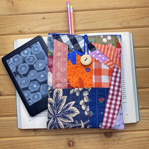 Peut inclure: Une housse de liseuse en tissu patchwork coloré avec un motif floral bleu, blanc et orange. La housse est dotée d'une fermeture à bouton et d'une sangle élastique bleue.