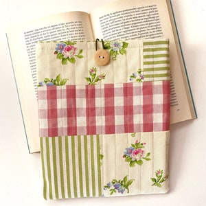 May include: A book cover made of patchwork fabric with a pink and white gingham pattern, green and white stripes, and a floral print. The cover has a button closure and is designed to protect a book.