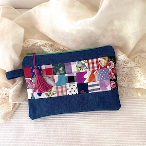 Può includere: Una pochette con cerniera in denim blu con un design a patchwork che presenta una varietà di tessuti colorati. La pochette ha un fiocco rosa attaccato al tiretto della cerniera.