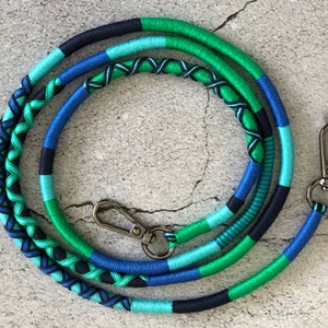 Könnte beinhalten: Ein geflochtenes Lanyard in Blau, Grün und Schwarz mit einem silbernen Drehverschluss. Das Lanyard besteht aus gewebtem Stoff und ist etwa 100 cm lang.