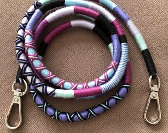 May include: A multi-colored braided cord with two silver clasps. The cord is made of purple, blue, black, and white yarn.