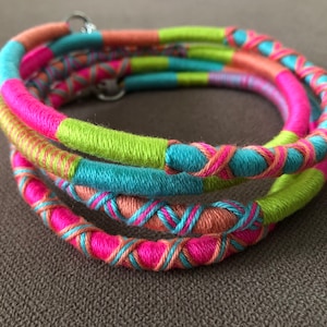 May include: Multicolored woven bracelet with pink, green, blue, and orange threads. The bracelet is made of several strands of yarn that are woven together to create a unique and colorful design.