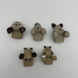 May include: Five ceramic animal figurines, each with a different animal face. The animals are an owl, a dog, a hippopotamus, a crocodile, and another dog. The figurines are all in a light brown color with brown and white accents.